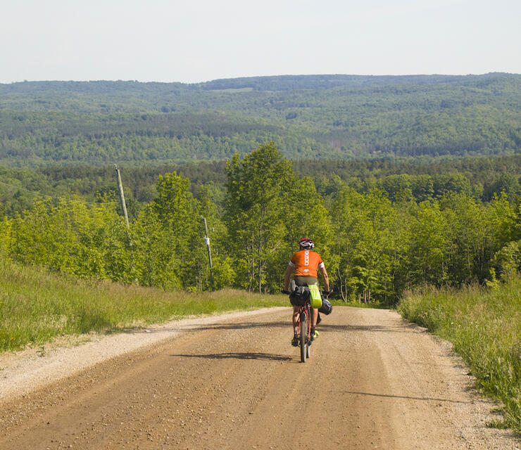 Cyclist riding on a gravel road, about to go down a big hill. 