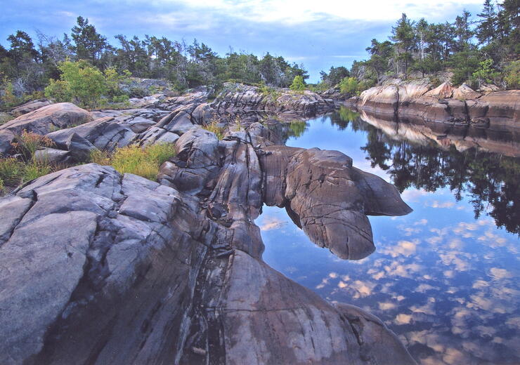 Beautiful rock lined shore of a river with reflection of clouds. 