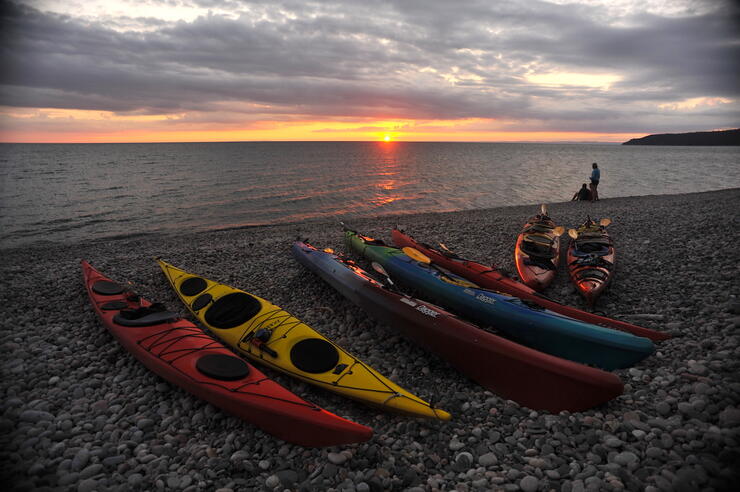 Kayaks on stone beach with sunset in background