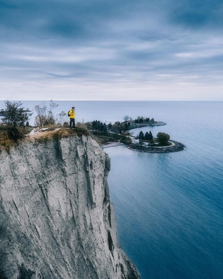 Person standing near edge of tall cliff overlooking Lake Ontario.
