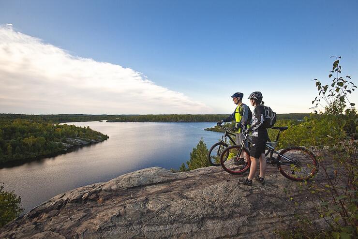 Couple of mountain bikers standing on rock overlooking lake