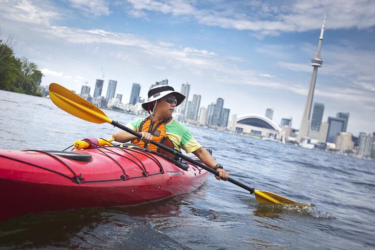 a man kayaks at the Toronto Islands with the city skyline behind him