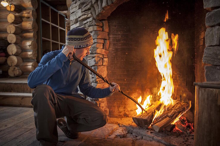 Man inside a log cabin stoking a wood fire