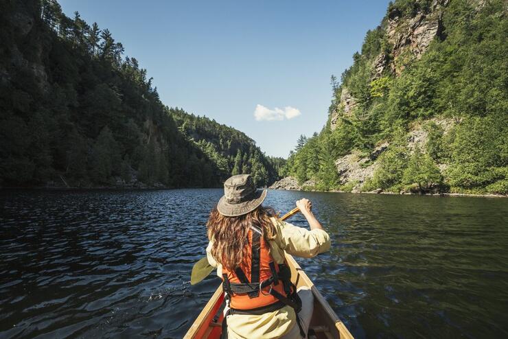 bow shot of a woman paddling a canoe downriver between steep rocky walls