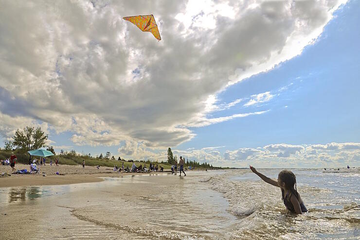 Young girl in shallow water on a beach, flying a kite