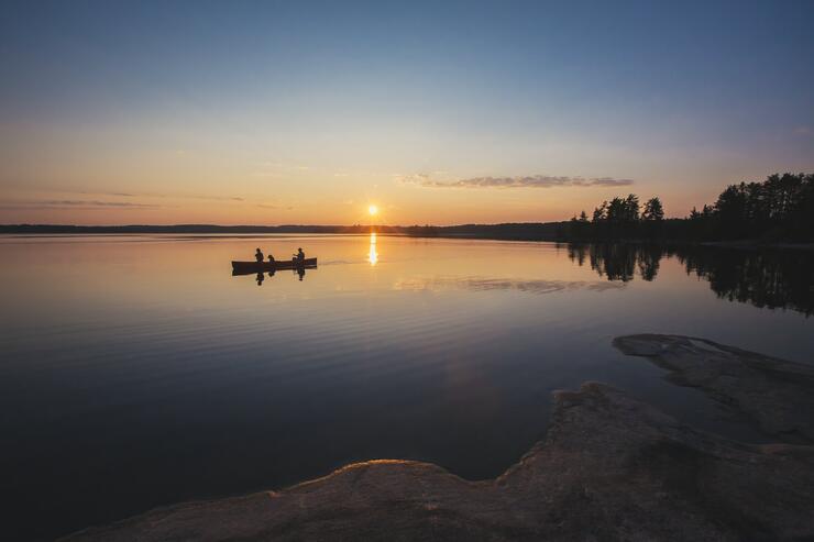 Two people paddling a canoe at sunset on a peaceful lake. 