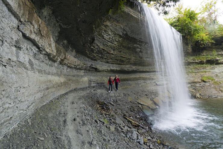 Two people walking behind a large waterfall 