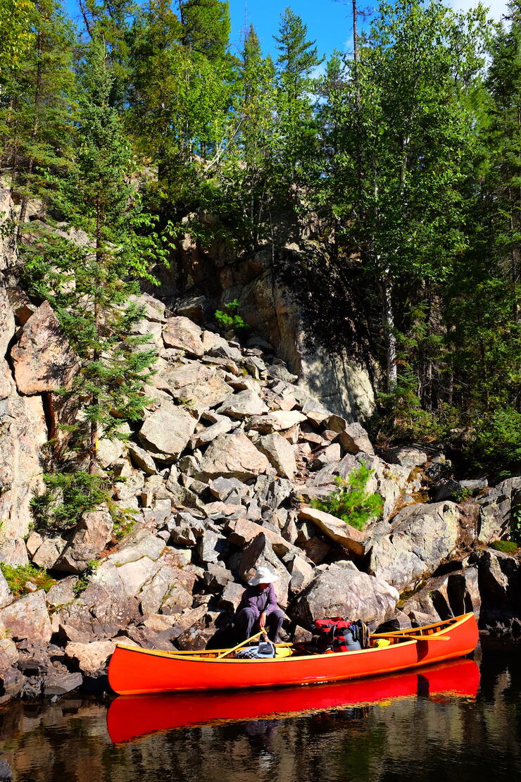 Man in red canoe at base of large boulder portage up a hill