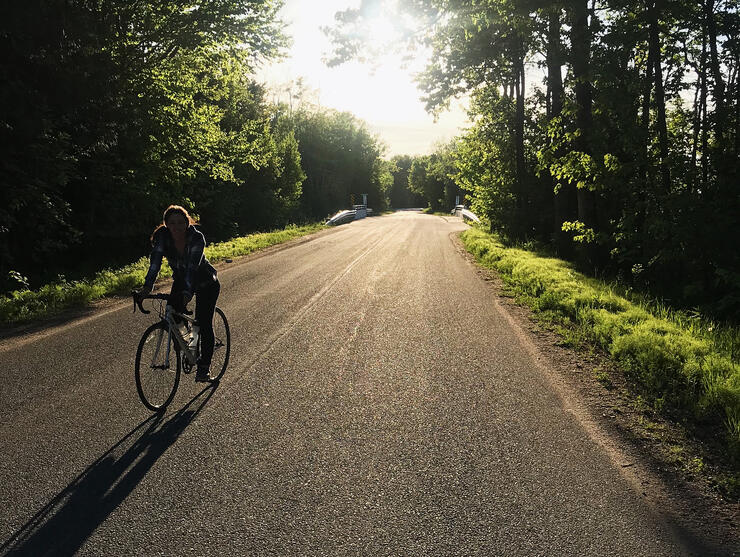 Cyclist riding on a quiet paved backroad with forest on each side. 