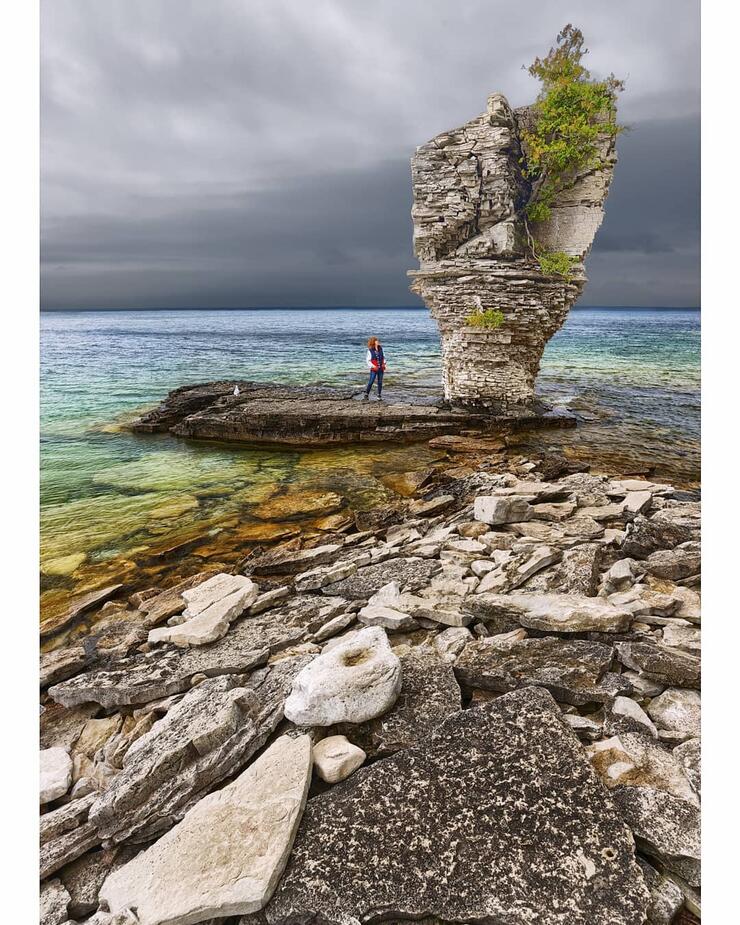 Woman standing beside flowerpot island rock formation. 