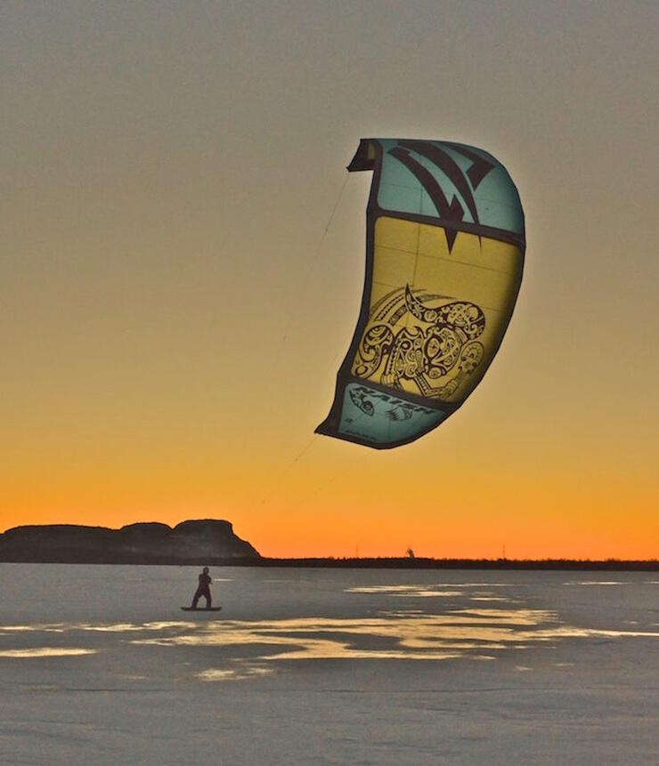 Person on a snowboard snowkiting at sunset