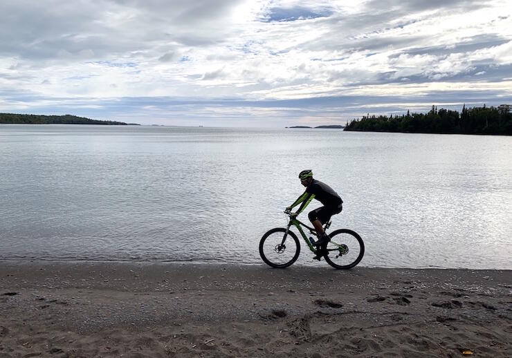 Man biking on beach beside a beautiful lake.
