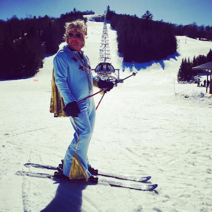 Man on skis dressed in power blue outfit with a cape.