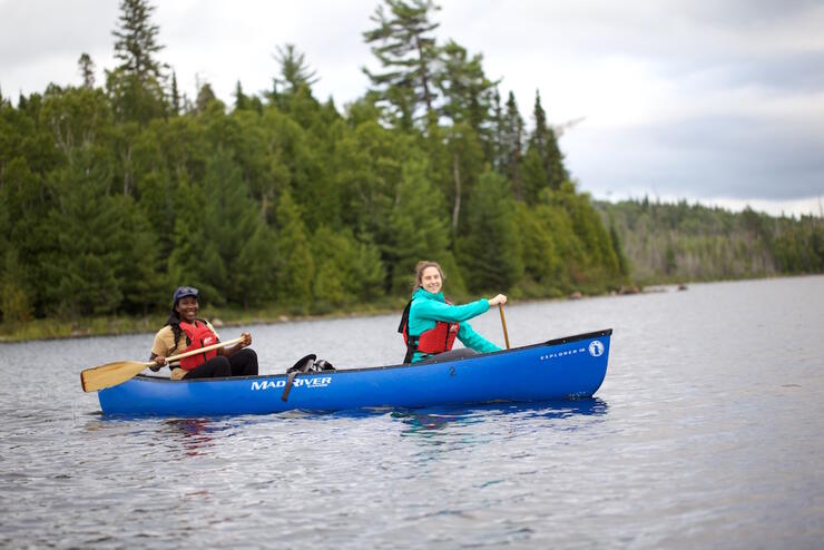 Two women paddling a blue canoe on a lake 