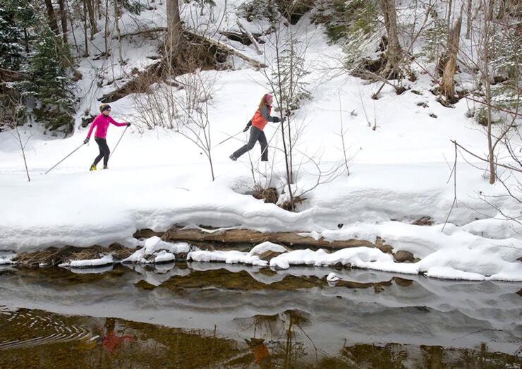 Two women skiing beside an open creek. 