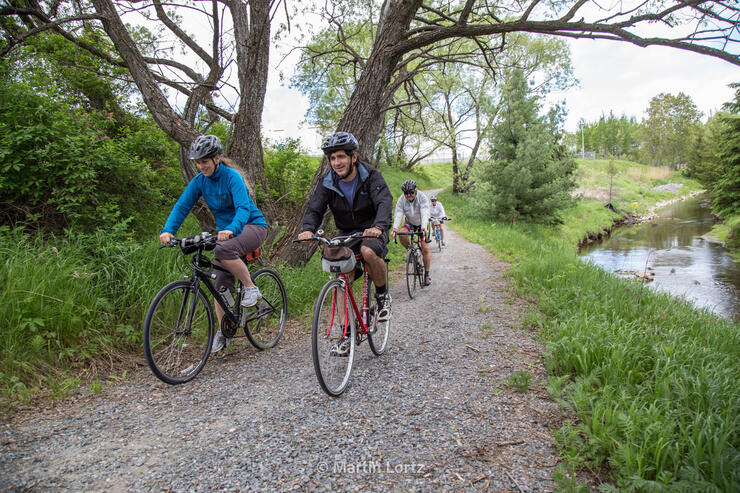 cyclists ride down a gravel path beside a stream