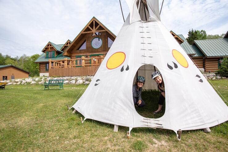 Two people wearing cycling helmets peaking out of a teepee