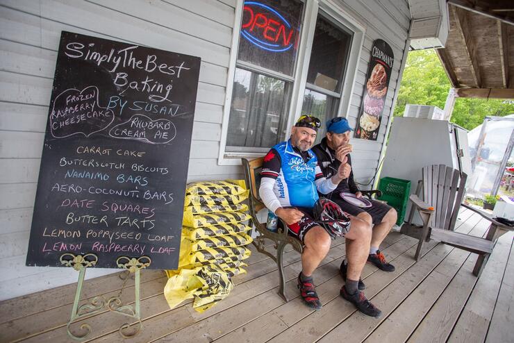 Two male cyclists sitting on a bench in front of a bakery