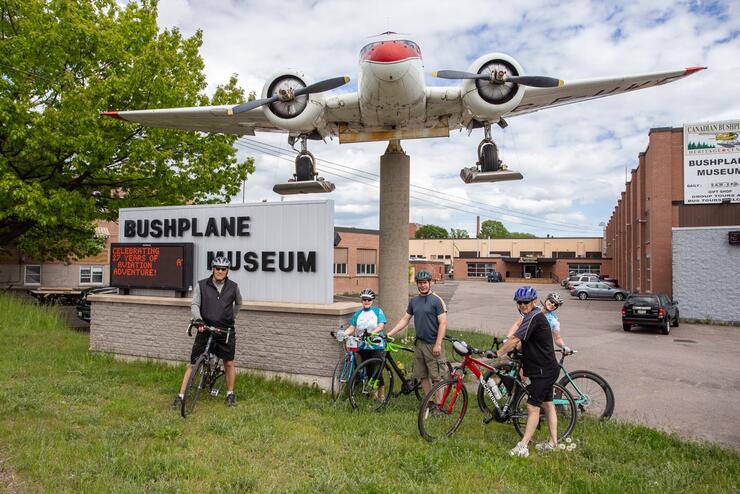 Four cyclists standing with bikes in front of Bushplane Museum 