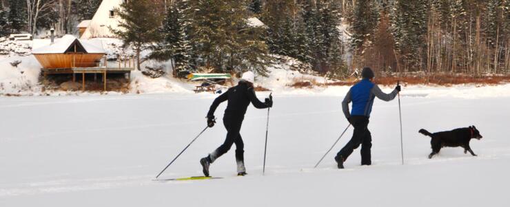 Two people cross country skiing on a lake in front of a yurt. 
