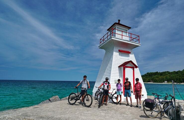 Cyclists standing with bikes in front of a lighthouse. 