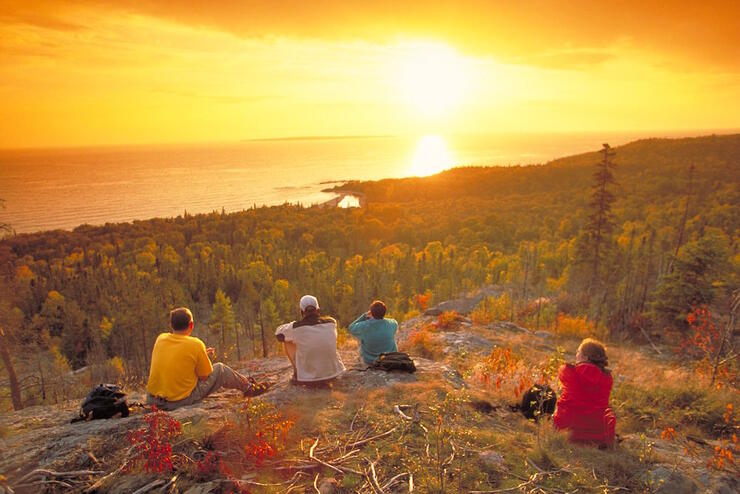 Several people sitting on a rock with a beautiful sunset view of Lake Superior