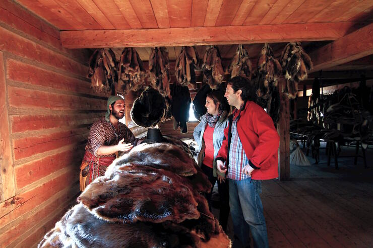 People looking at pile of furs in a log cabin. 