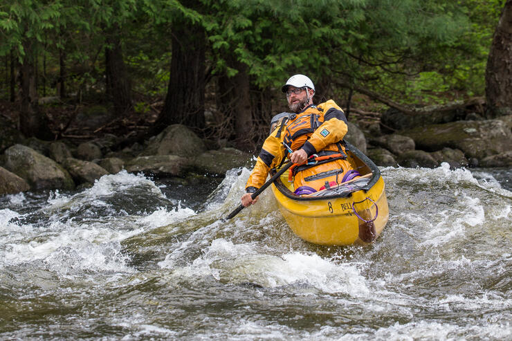 Man paddling a yellow canoe in whitewater 