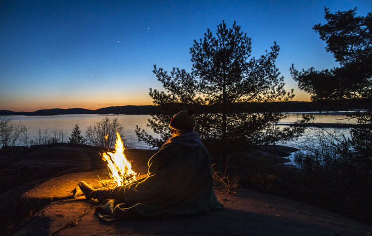 Person sitting at campfire at sunset. 