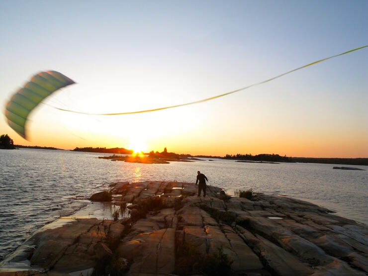 kite flying over rocky point with sun setting 
