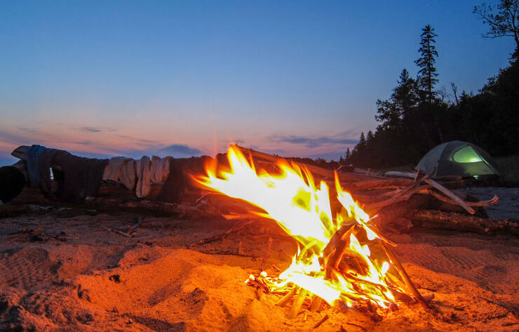 Campfire on sandy beach with tent in background