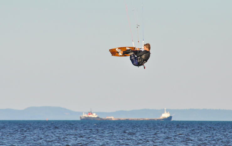 Man flying over water on a kiteboard. Ship in background