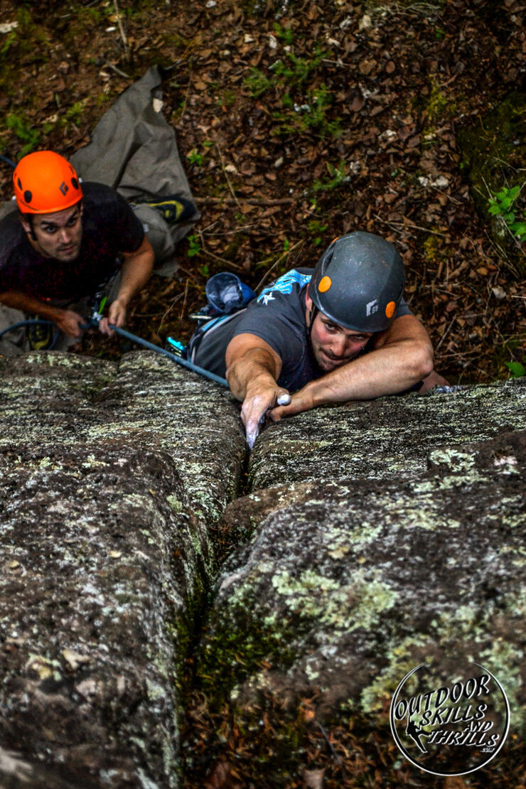 Man reaching for a hold in a crack on vertical rock face.