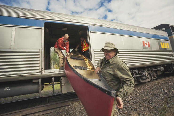 Man helping to unload a red canoe from a Via Rail Train. 