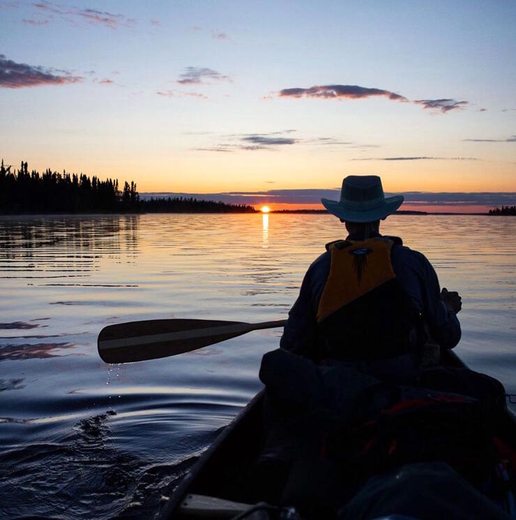 Man paddling in bow of canoe at sunset. 