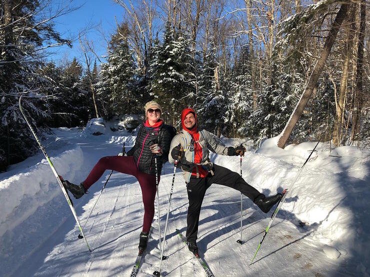 Two cross-country skiers holding up one ski. 