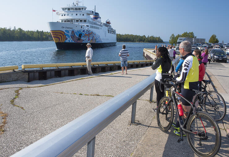 Cyclists standing with bicycles looking at MS Chi-Cheemaun. 