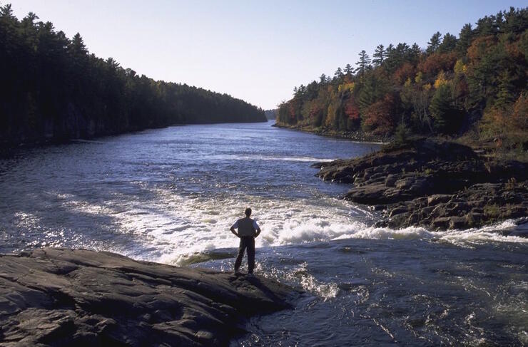 Man standing on a smooth rock looking at falls and river