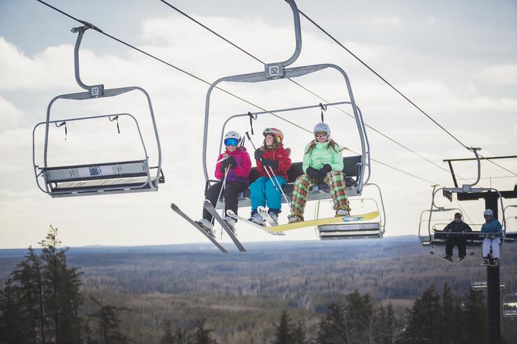 People with skiis on riding in a chair-lift. 