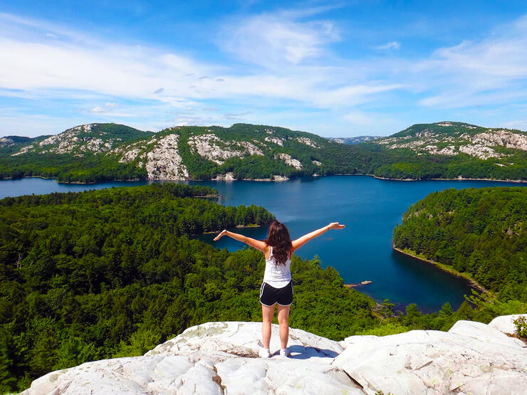 Woman standing on top of a cliff overlooking turquoise lakes and white mountains.