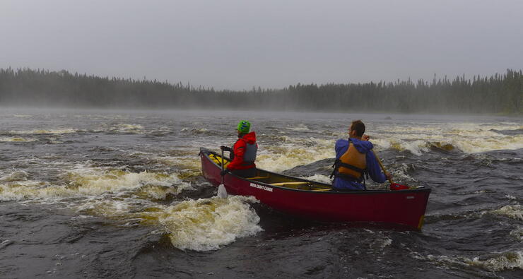 Two canoeists in red canoe paddling in whitewater. 