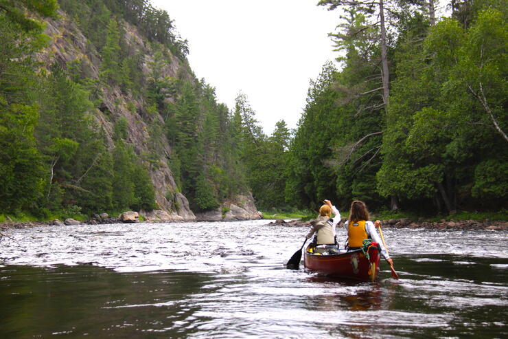 Two women paddling a red canoe down a river. 