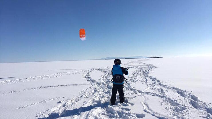 Child standing on frozen lake holding a kite. 