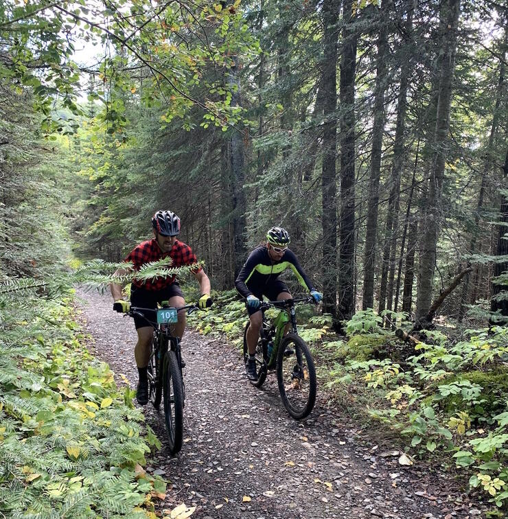 Two mountain bikers riding on a gravel trail in forest.