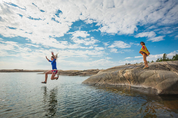 Woman jumping into the water from a rock with other woman watching