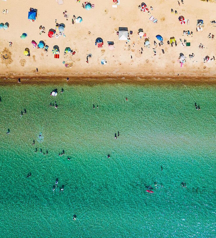 Aerial view of sandy beach and turquoise waters with lots of people.