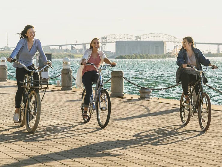 Three people cycling on waterfront boardwalk. 