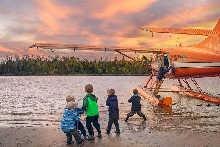 Group of kids on a beach holding a rope tied to a floatplane. 