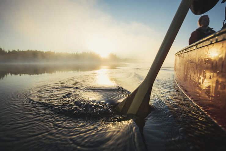 Side of a canoe and paddle in water at sunrise