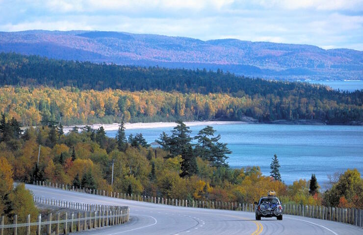 Car with bike on back travelling down highway beside Lake Superior